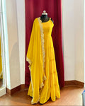 Yellow Anarkali with golden border on a mannequin against a red curtain.