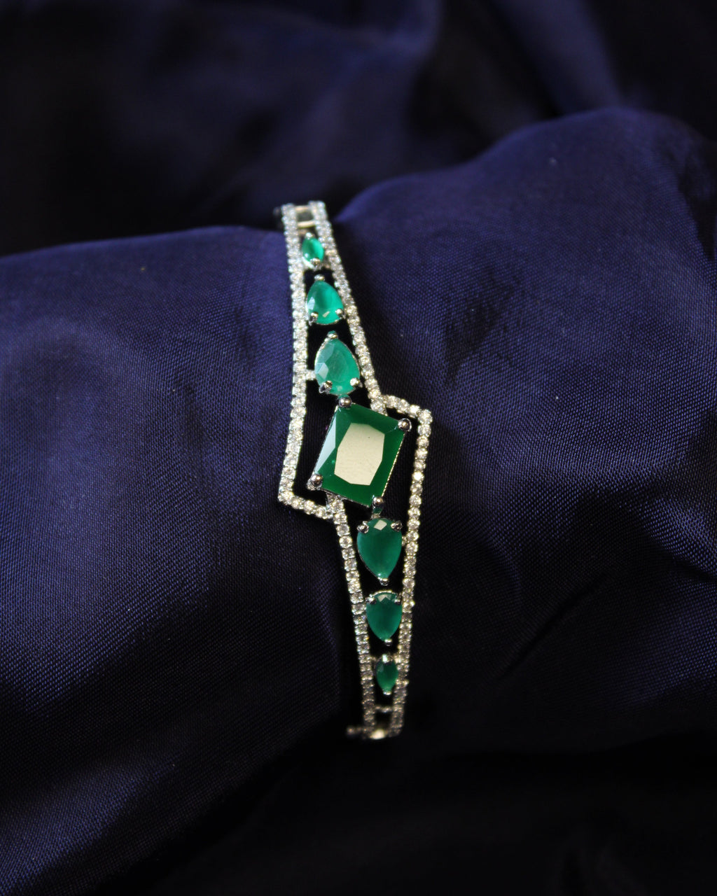 Green emerald gemstone bracelet on a dark blue fabric background