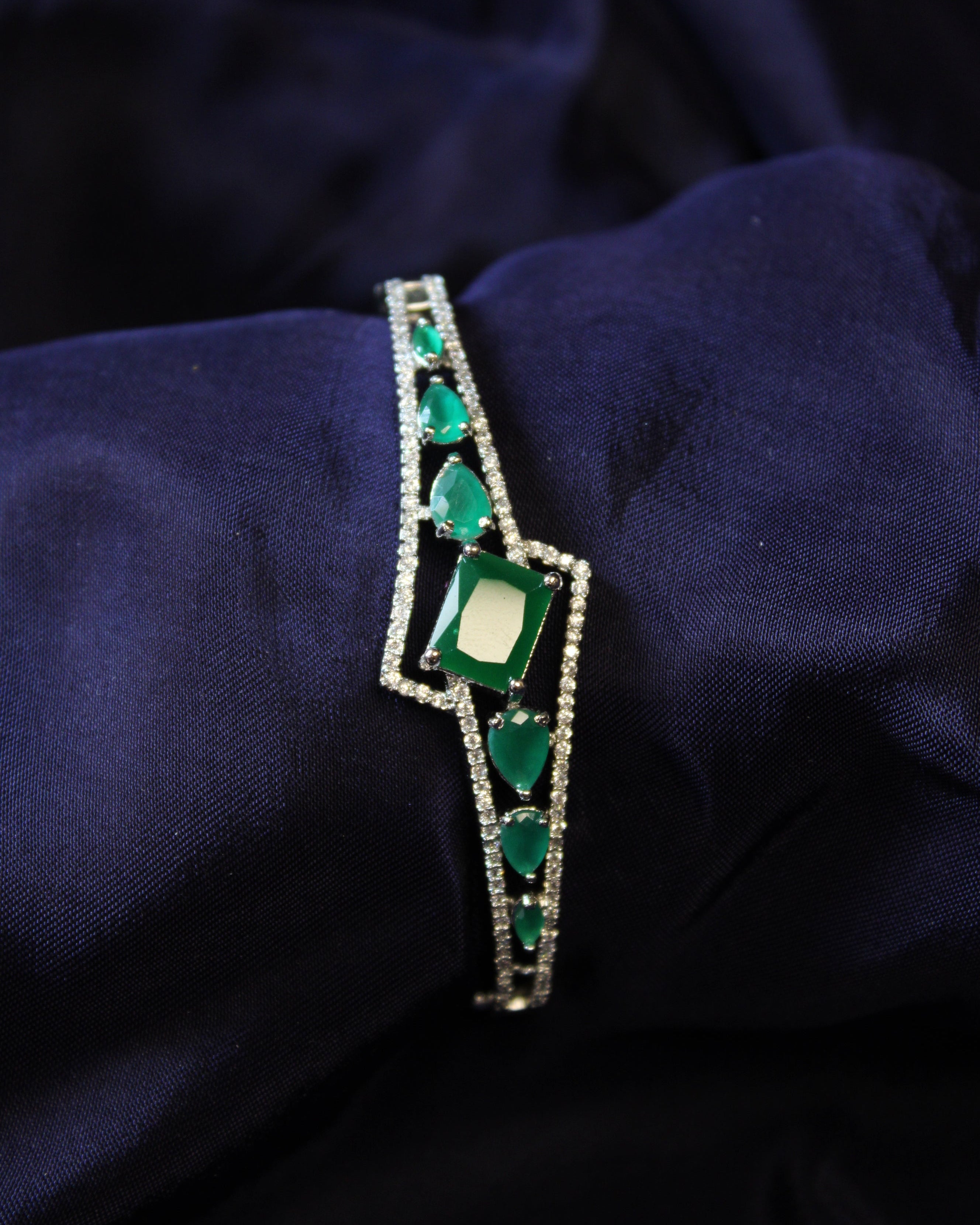 Green emerald gemstone bracelet on a dark blue fabric background
