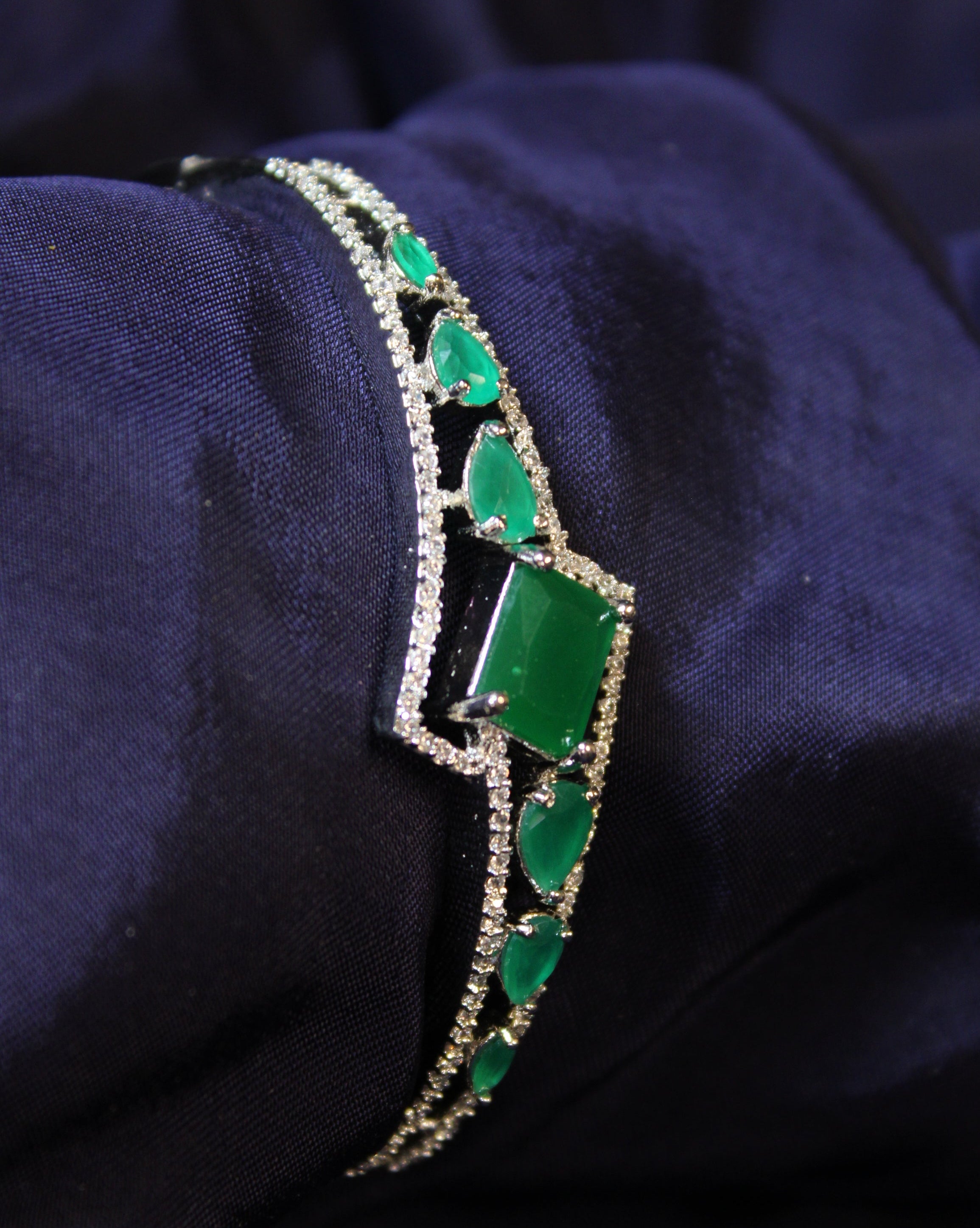 Green emerald gemstone bracelet with silver accents on a dark fabric background
