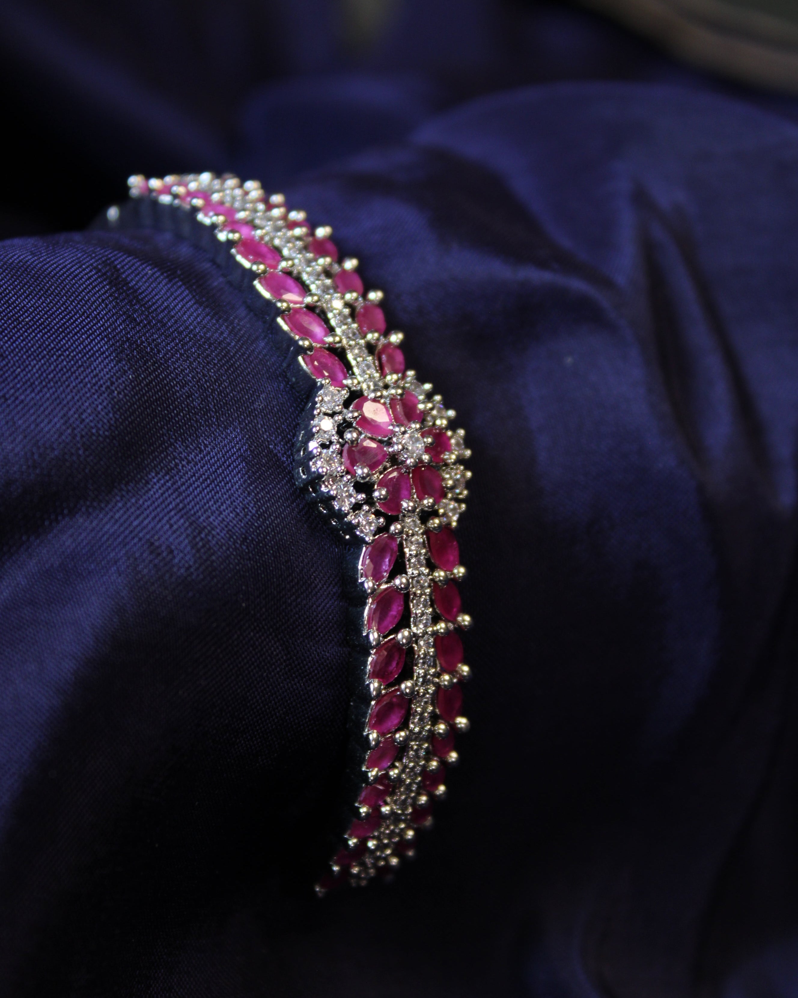 Jeweled bracelet with red ruby stones on a dark blue fabric background
